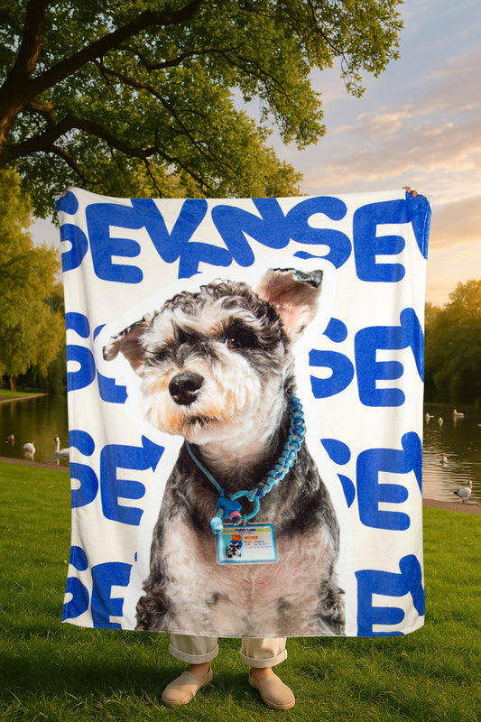 Person holding a blanket with a dog's face and 'Evans' printed on it in a park setting.