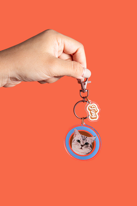 Hand holding a keychain with a cat's face on an orange background