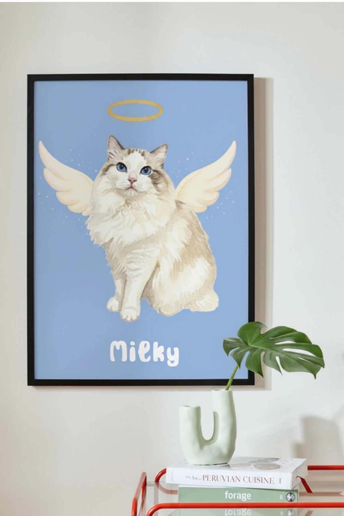 Framed artwork of a cat with angel wings and halo labeled 'Milky' on a wall.