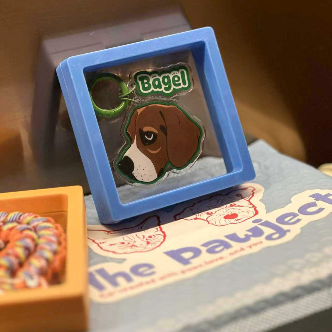 Dog tag with a paw print design on a blue stand, placed on a surface with a branded mat.