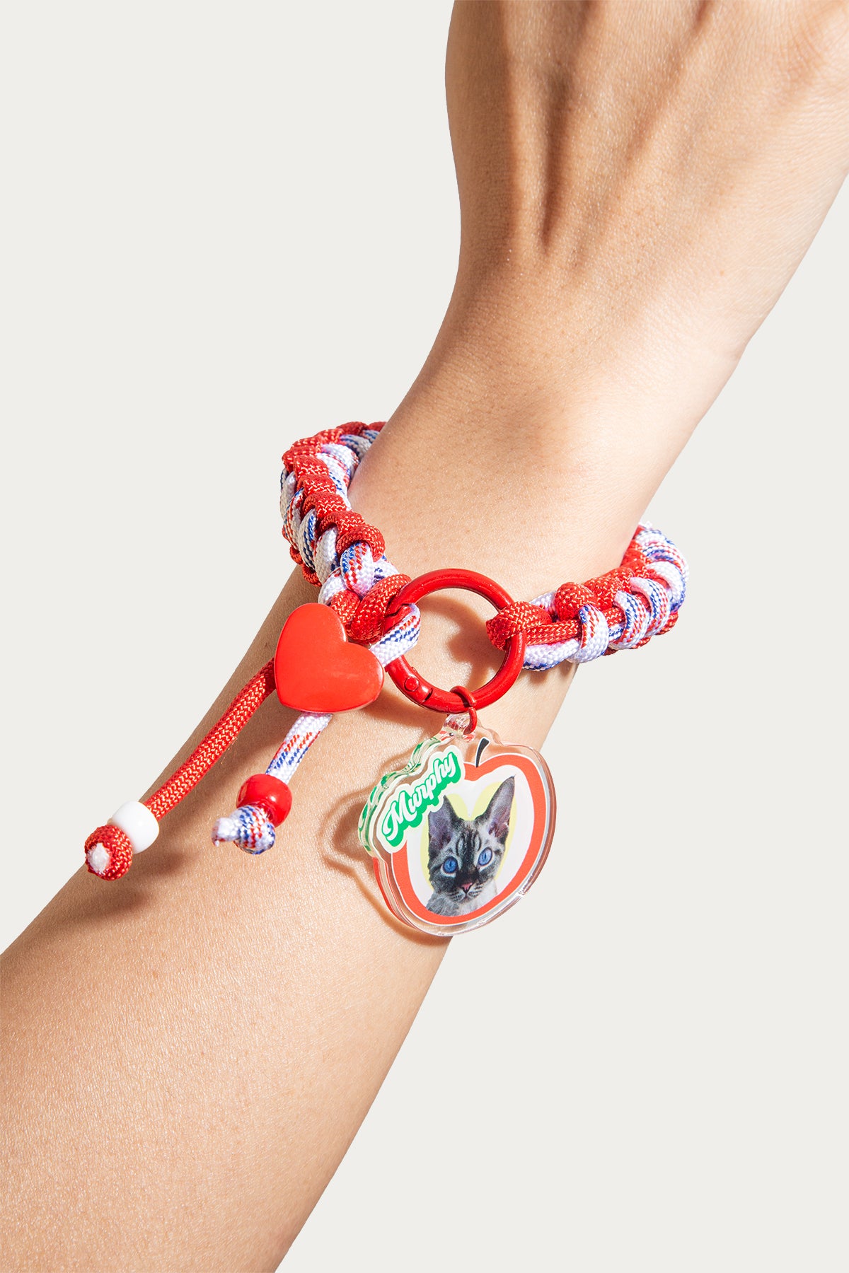 Bracelet with heart and cat charm on a wrist against a neutral background
