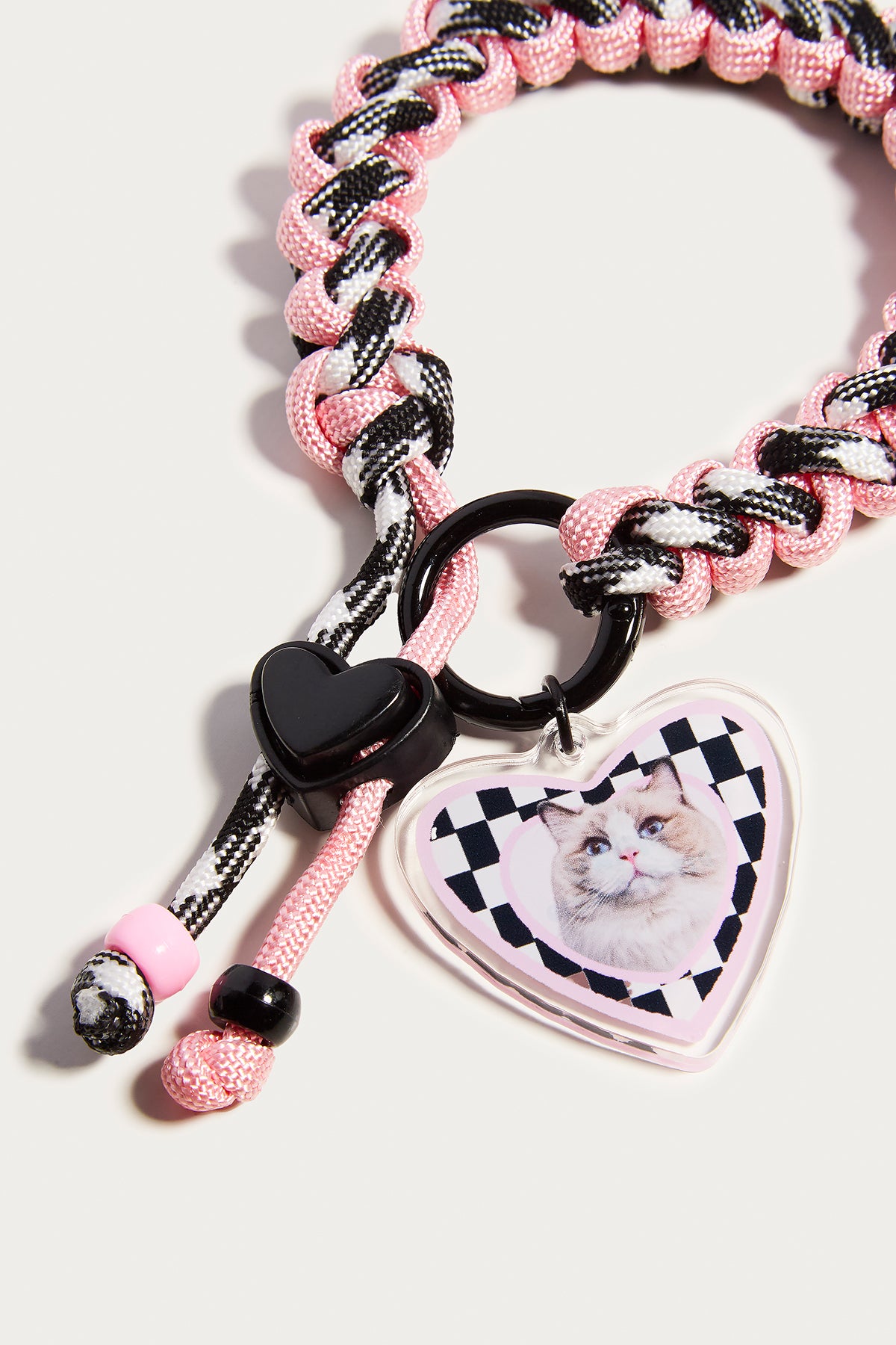 Pink and black braided keychain with heart-shaped tag featuring a cat illustration on a white background