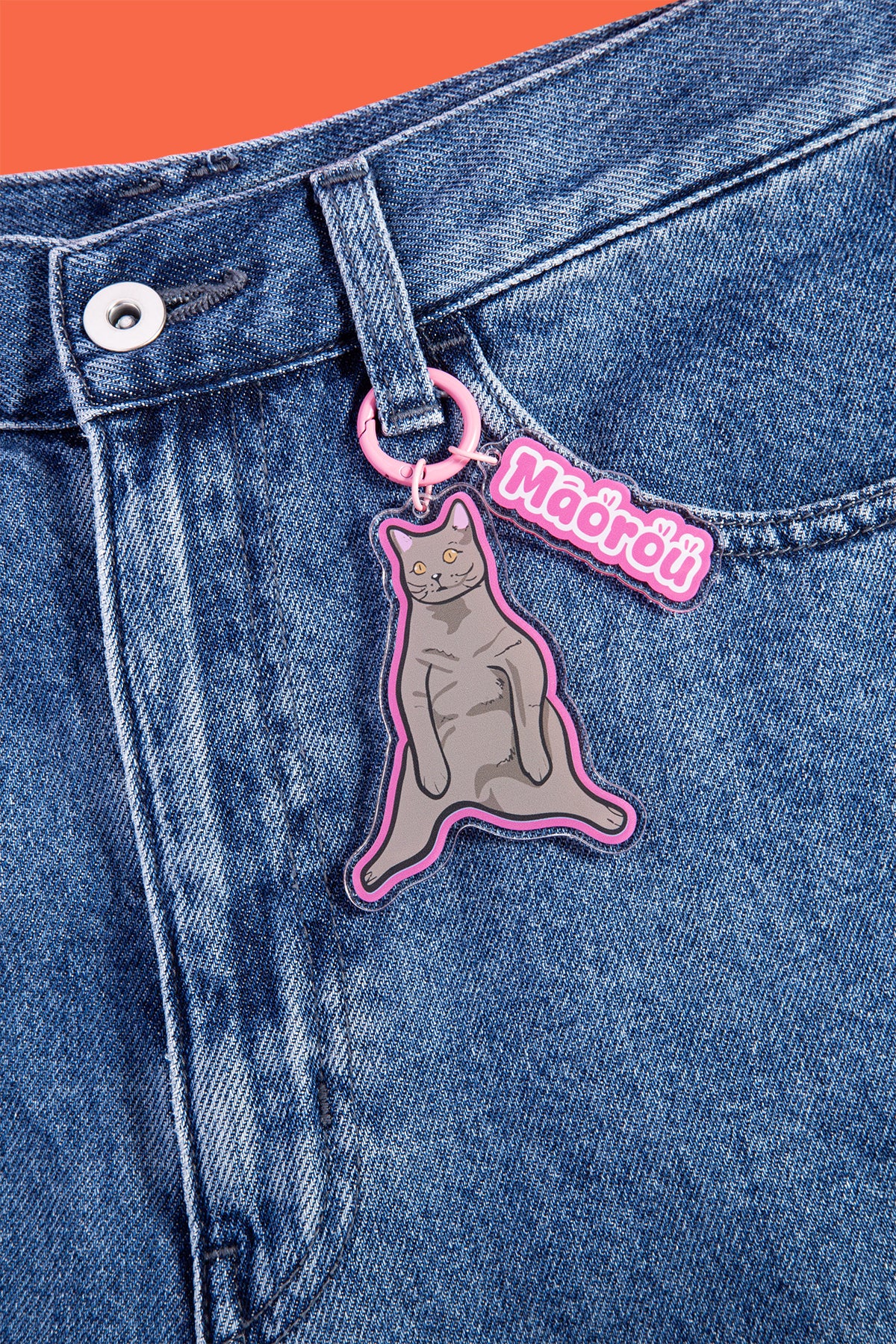 Cat-shaped keychain with 'Miaou' tag attached to a blue denim jacket.
