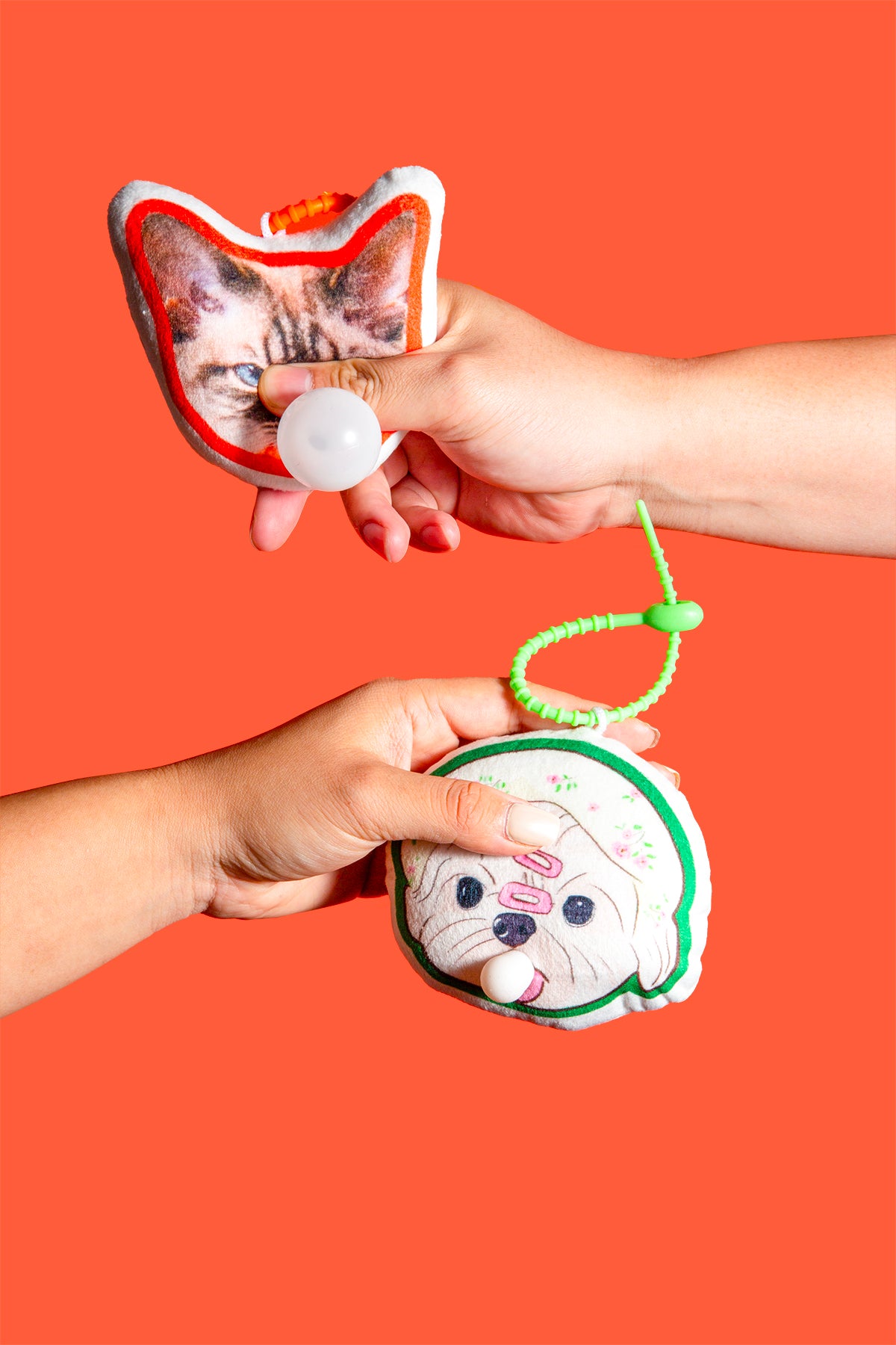 Two hands holding cat-themed toys against an orange background