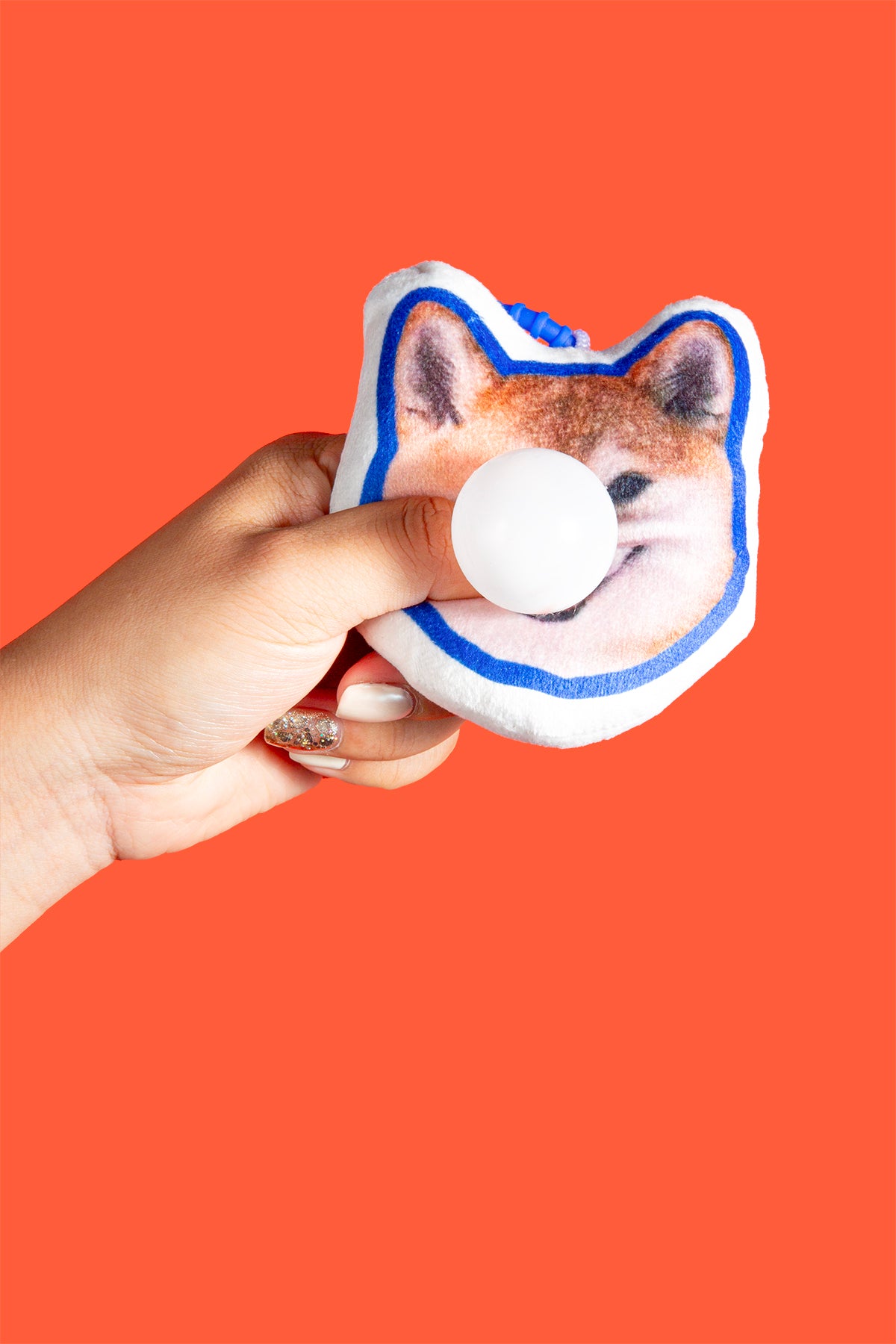 Hand holding a dog-shaped stress ball against an orange background