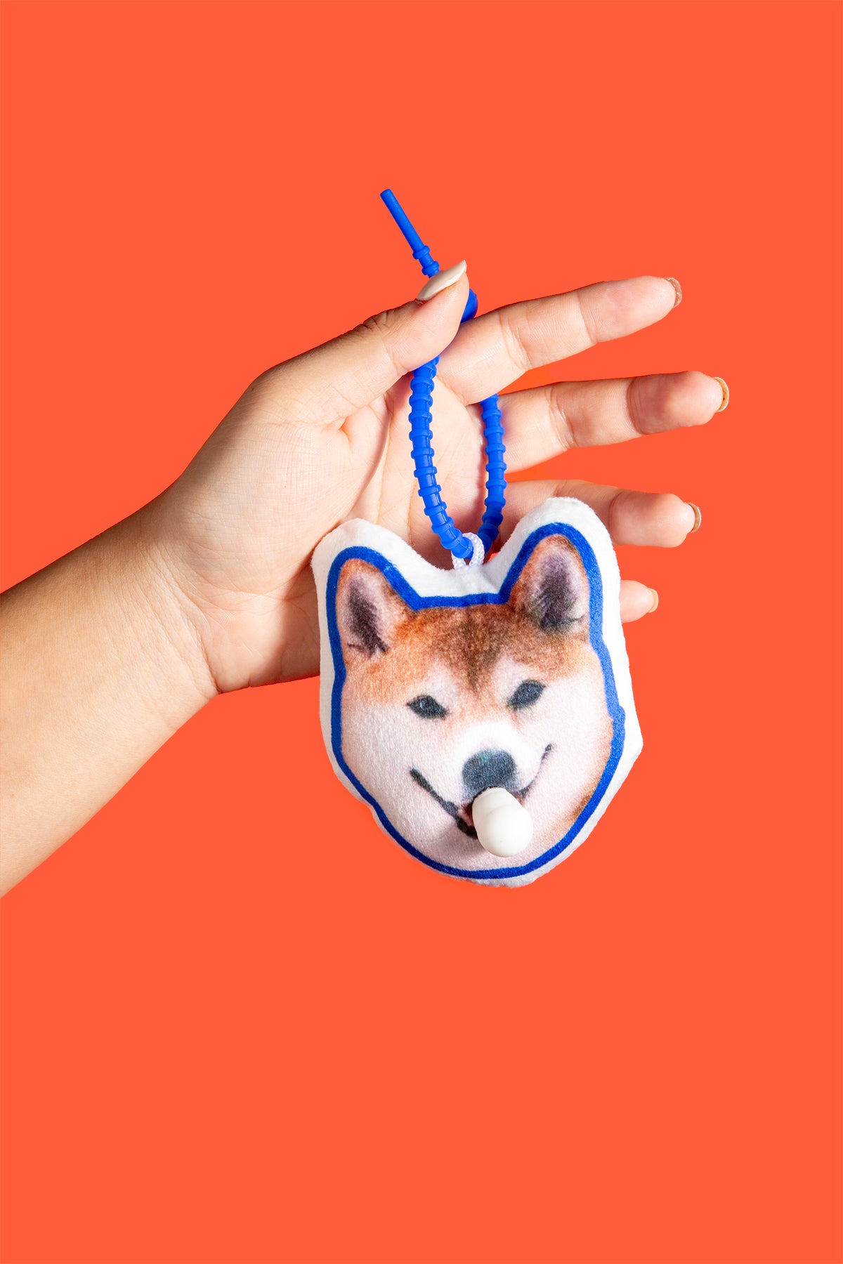 Hand holding a dog-shaped keychain against an orange background