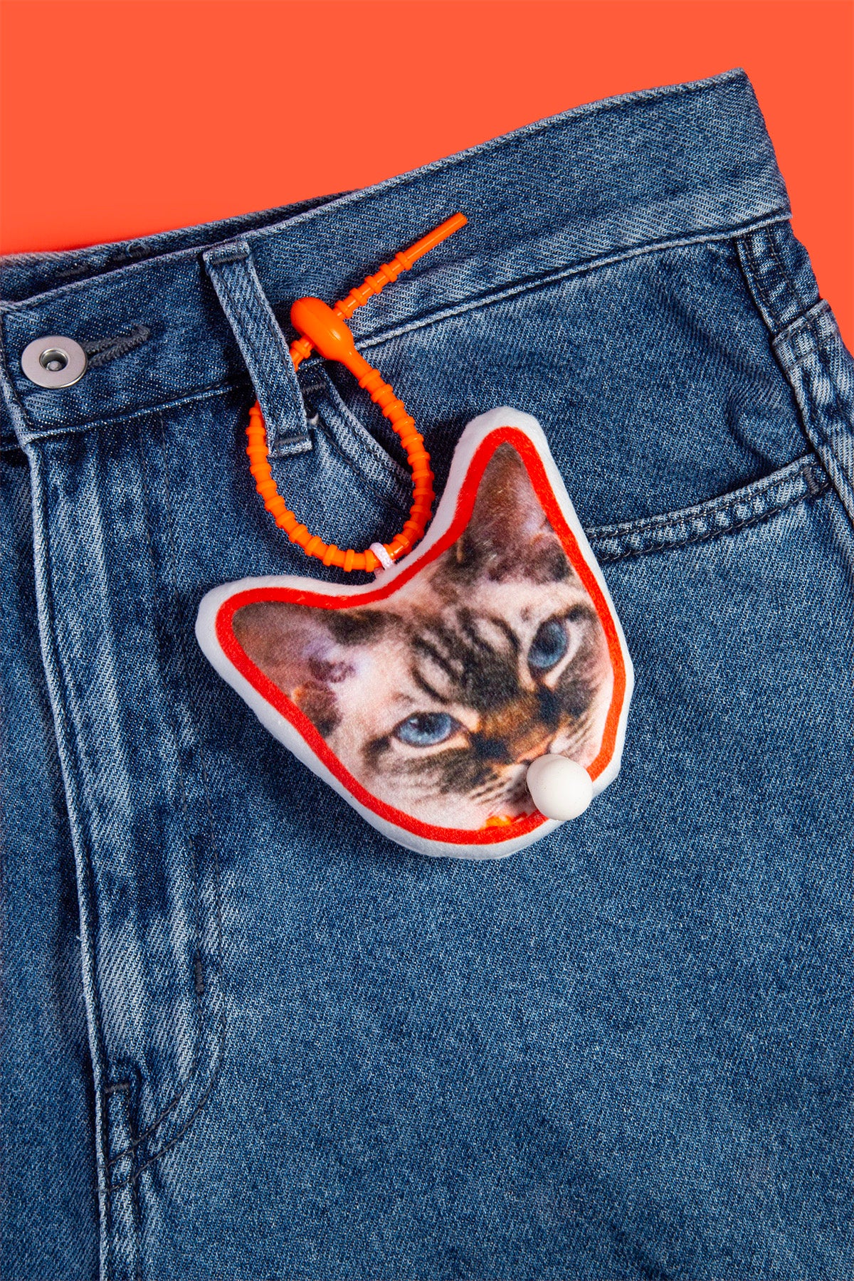 Cat-shaped keychain with a cat's face on blue jeans against an orange background