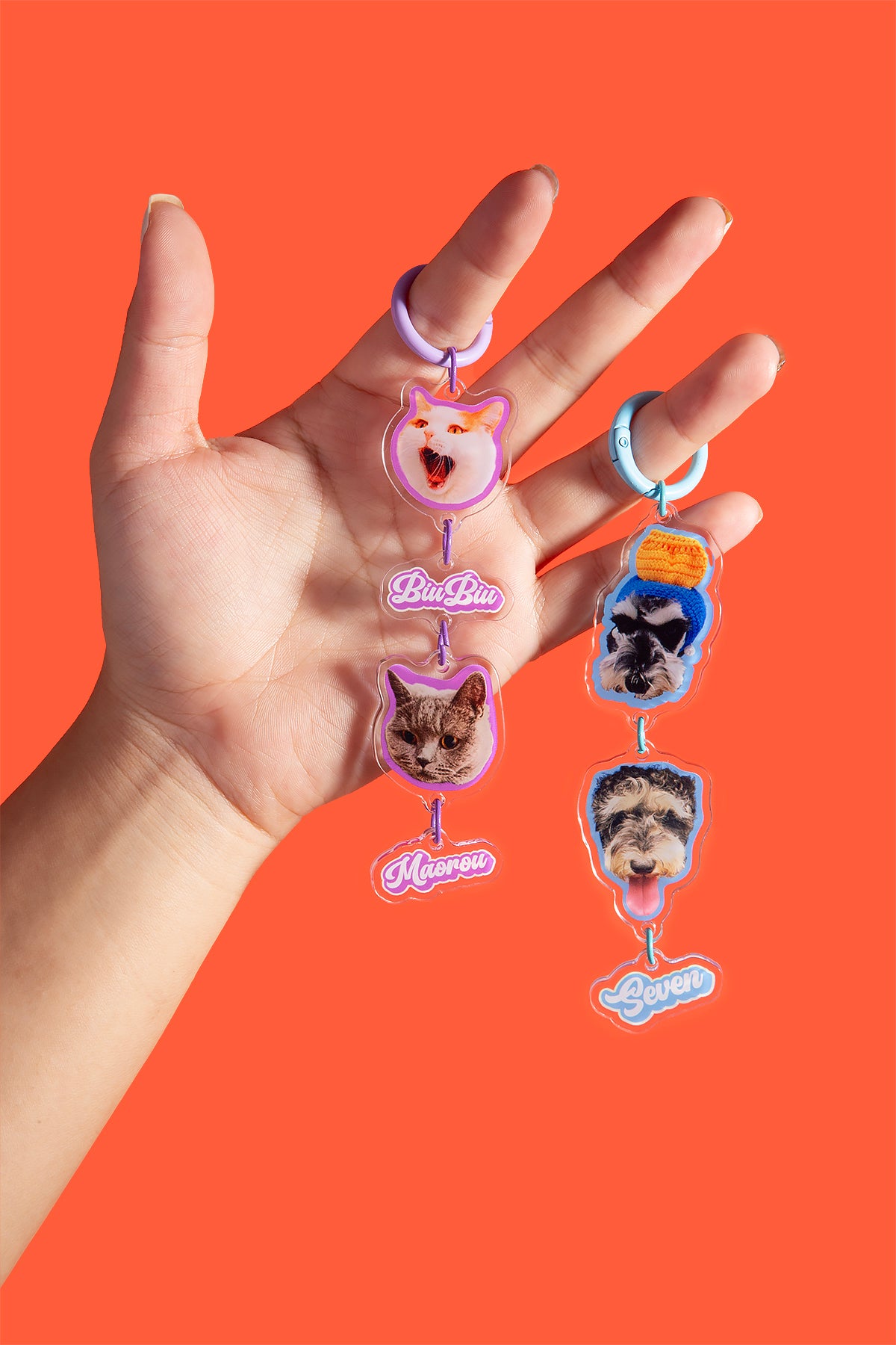 Hand holding a keychain with cat-themed charms against an orange background
