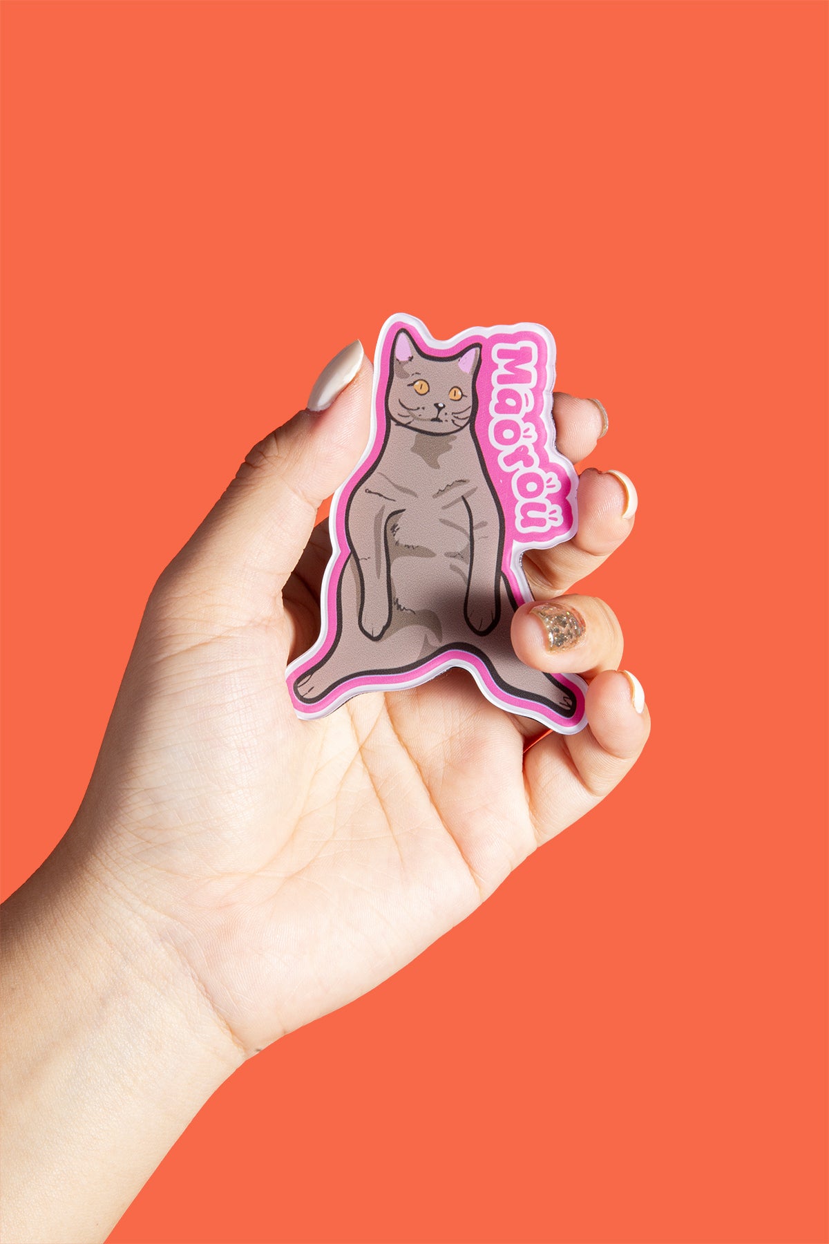 Hand holding a cat-shaped sticker with 'Meow' text on an orange background