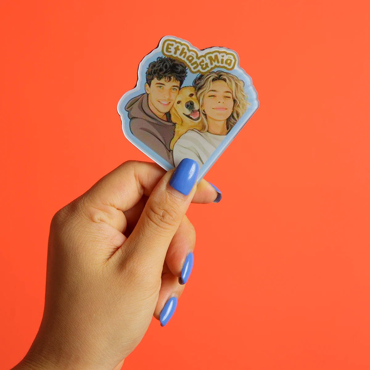 Hand holding a sticker with two people and a dog against an orange background