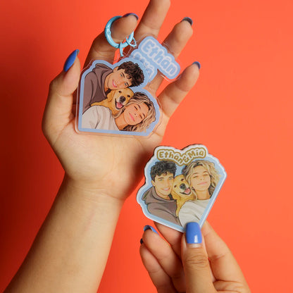 Hand holding two keychains with illustrations of people and a dog against an orange background