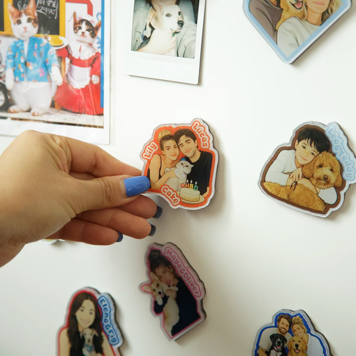 Hand holding a sticker with a couple and dog, surrounded by other similar stickers on a white surface.