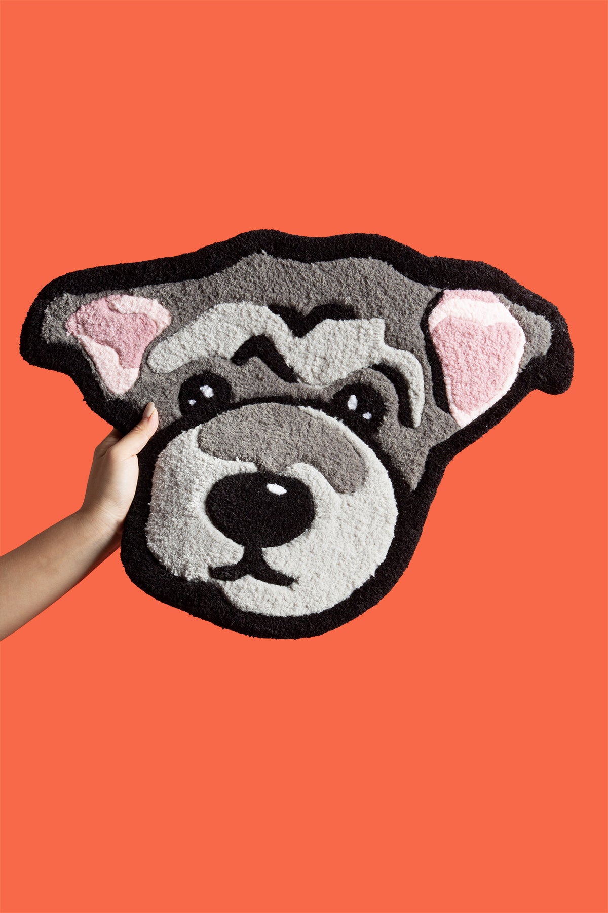 Dog-shaped rug with a hand touching it against an orange background
